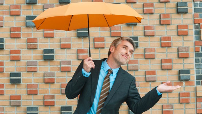 Mann mit Knirps-Regenschirm vor bunter Steinmauer