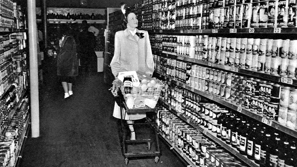 Frau schiebt gefüllten Einkaufswagen durch US-Supermarkt (s/w, 1940)