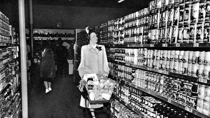 Frau schiebt gefüllten Einkaufswagen durch US-Supermarkt (s/w, 1940)