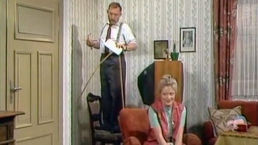 Alfred Tetzlaff(Heinz Schubert) steht auf einer Leiter mit Bandmaß, Else Dorothea Tetzlaff(Elisabeth Wiedemann) sitzt auf einem Sessel und lächelt