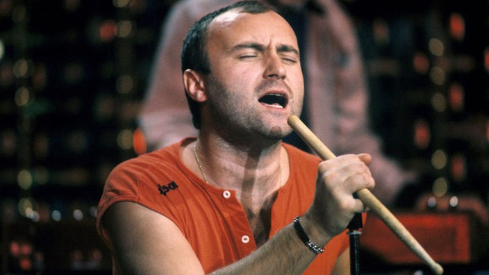 Phil Collins performt auf der Bühne: Singt in einen Drumstick