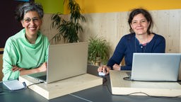Zwei Frauen sitzen vor tragbaren Computern