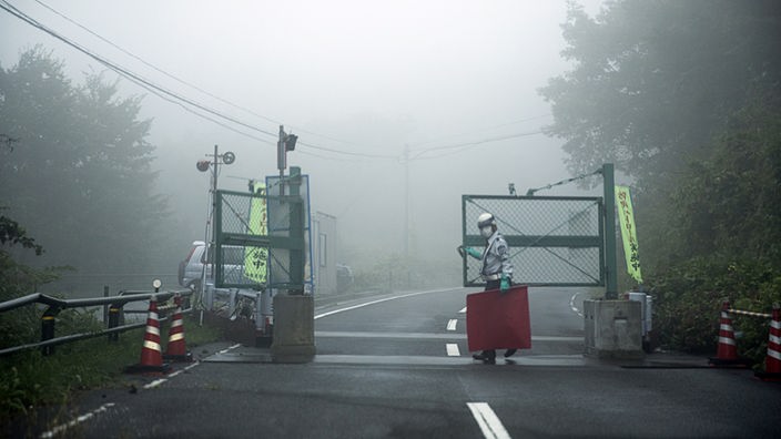 Straßensperre mit Warnhütchen, Mann in Schutzkleidung schließt ein Tor