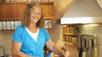 Barbara Büsch steht in ihrer Küche am Herd und lacht.