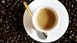 Das Bild zeigt eine Tasse mit Kaffee auf Kaffeebohnen.