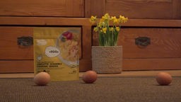 Das Bild zeigt drei Eier. Im Hintergrund ist ein veganes Ei-Ersatzprodukt abgebildet.