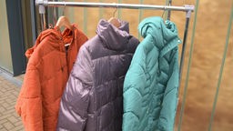 Drei Outdoor-Jacken hängen auf einer Kleiderstange.