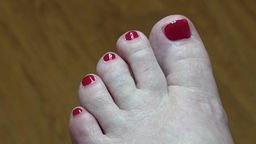 Ein linker Fuß mit rot lackierte Fußnägeln