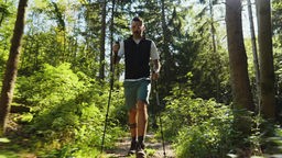 Ein Mann wandert mit Wanderstöcken im Wald