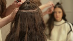 Das Bild zeigt eine Frau beim Friseur mit Extensions in ihren Haaren.