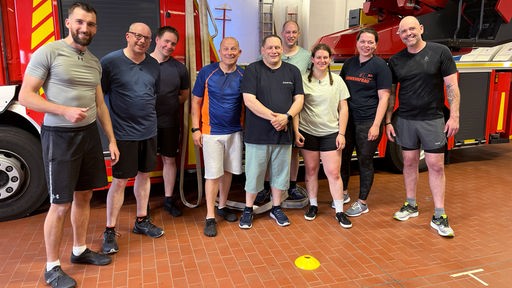 Das Bild zeigt Doc Esser (r), Sportcoach Marwin Isenberg (l) und das Team der Freiwilligen Feuerwehr aus Radevormwald.