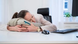 Eine junge Frau schläft am in einem Büro am Schreibtisch.