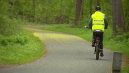 Ein Mann mit Warnweste fährt mit seinem E-Bike durch den Wald