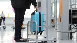 Das Bild zeigt eine Person, die ihr Handgepäck wiegt. 