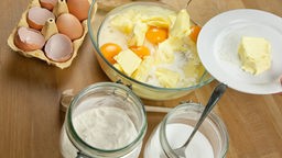 Eine Frau gibt Butter in eine Rührschüssel mit Mehl, Zucker und Ei, um einen Rührteig anzufertigen.
