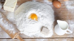 Mehl zu einem Haufen aufgeschüttet - in einer Mulde befindet sich ein aufgeschlagenes Ei.