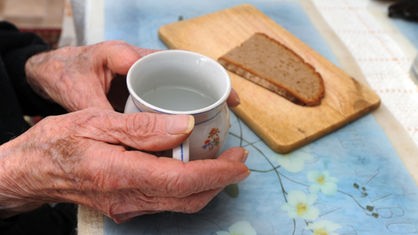 Alter Mensch sitzt vor einer Tasse und einer Scheibe Brot