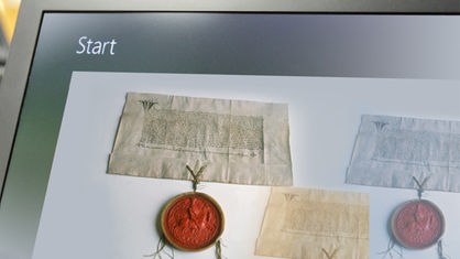 Ein Computerbildschirm und ein altes Dokument mit rotem Siegel