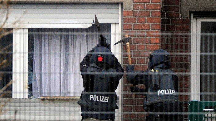 Mit Axt und  Machete öffnen zwei Polizisten einen Fensterladen 
