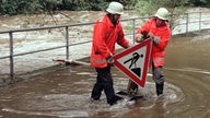 Feuerwehrleute bergen im September im Eifel-Städtchen Monschau ein Baustellenschild von einer überfluteten Straße neben der Rur, 1998