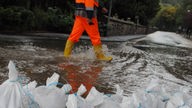 Ein Arbeiter geht in Bad Münstereifel hinter einer Wassersperre aus Sandsäcken über eine durch den Fluss Erft überschwemmte Straße