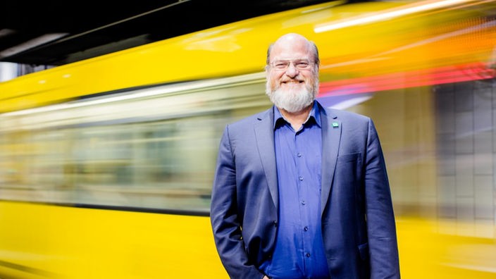 Grünen-Politiker Rolf Fliß vor einer gelben Bahn. Fliß wurde in Essen angegriffen.