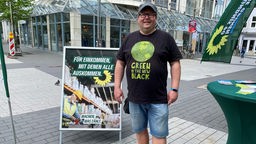 Oliver Buschmann am Grünenstand in der Bochumer Innenstadt neben einem Wahlplakat
