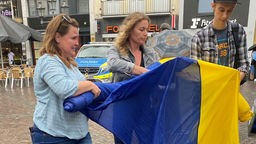 Zwei Frauen und ein Mann rollen eine große ukrainische Fahne aus.