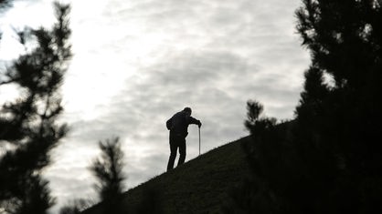 Ein älterer Mann mit Gehstock besteigt einen Hügel