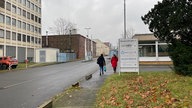 Ein Schild mit Firmen Namen und zwei Frauen im Hintergrund 