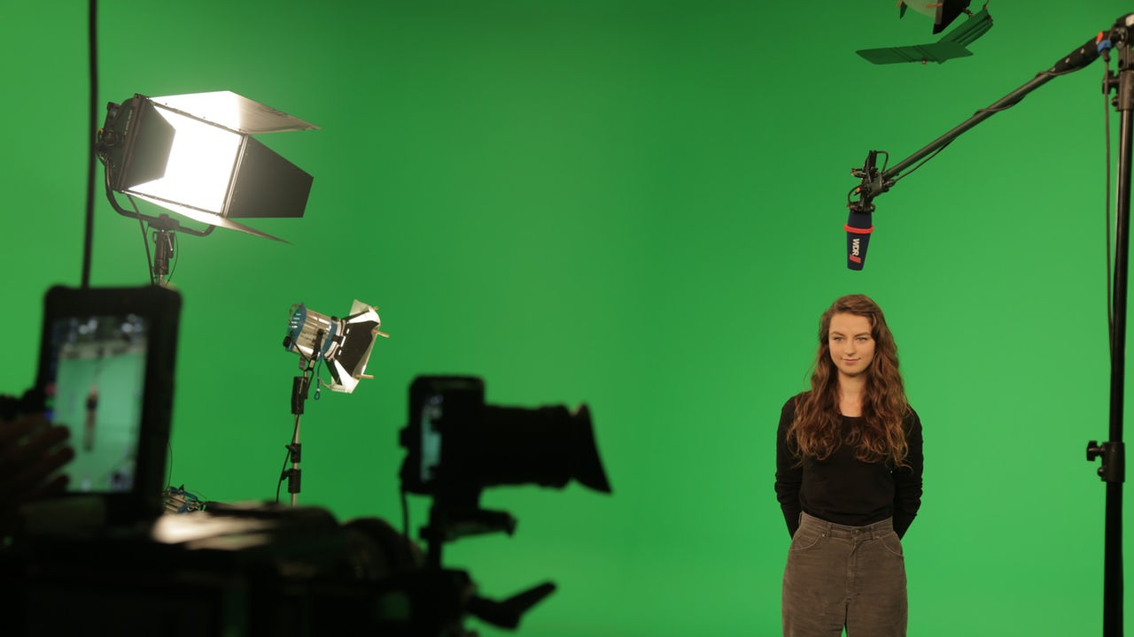 Eine junge Frau steht in einem Studio mit komplett grünem Hintergrund