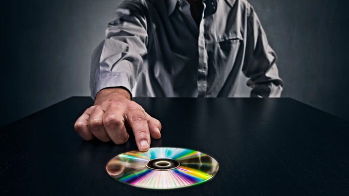 Mann schiebt CD über einen Tisch (Symbolfoto)