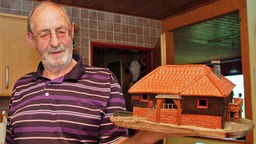 Mann blickt auf ein Ton-Modell eine Hauses