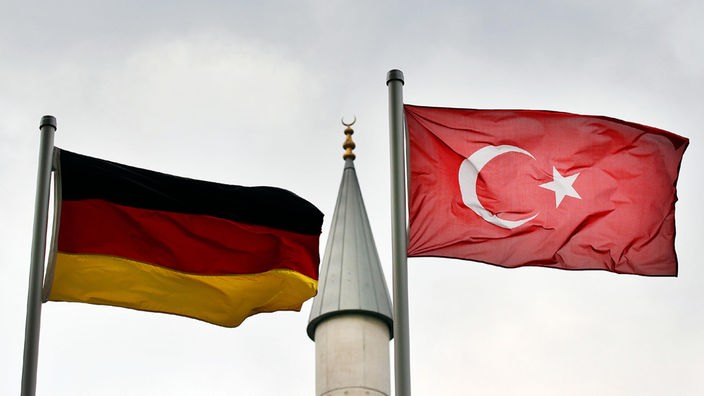 Eine deutsche und eine türkische Fahne wehen vor dem Minarett einer Moschee