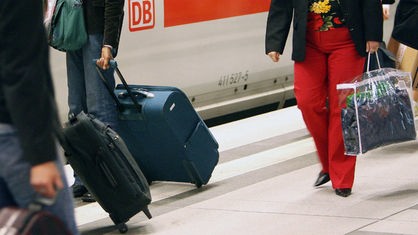 Reisende gehen mit Gepäck über einen Bahnsteig im Bahnhof