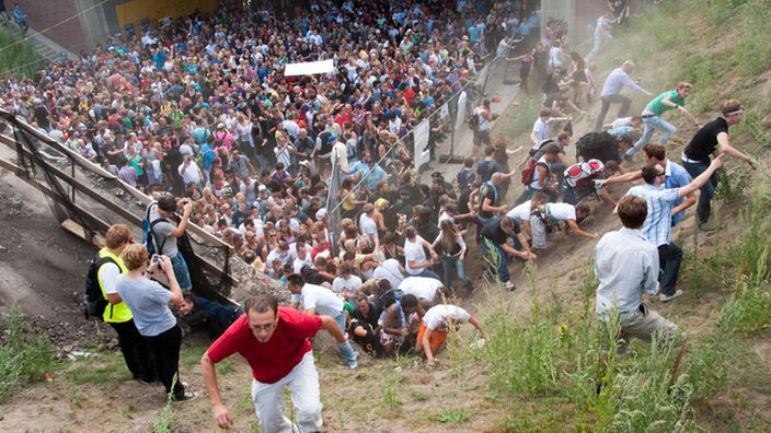 Menschen fliehen bei der Loveparade 2010 eine Böschung hinauf