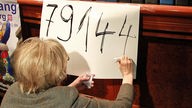 Eine Mitarbeiterin der Bürgerinitiative Neuanfang für Duisburg schreibt die Zahl 79144 auf ein Schild 