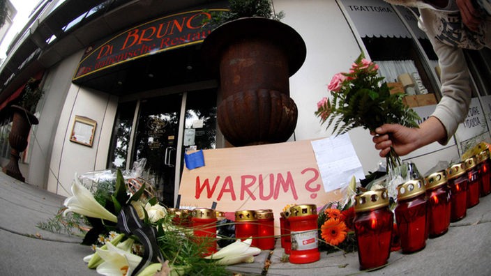 Kerzen und ein Schild mit "Warum?" vor der Pizzeria Da Bruno