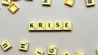 Der Schriftzug 'Krise' liegt auf einem Tisch zwischen anderen Spiele-Buchstaben