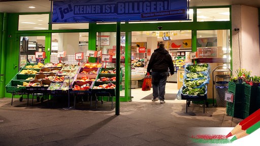 Eine Person tritt über die Schwelle eines beleuchteten  Supermarktes