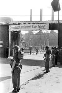 Britische Soldaten 1949 am Eingang der Ruhrchemie AG in Oberhausen, darüber ein Transparent mit dem Satz "Demonteure, nun beginnt Euer Werk!"