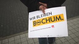 Ein Mitarbeiter von Opel hält am Samstag (16.06.2012) nach einer Belegschaftsversammlung ein Schild mit der Aufschrift "Wir bleiben Bochum"