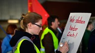 Eine Arbeiterin schreibt vor dem Tor 4 des Opel-Werks in Bochum am Rande einer Betriebsversammlung den Schriftzug "Wir stehen hinter Euch!" auf ein Plakat.