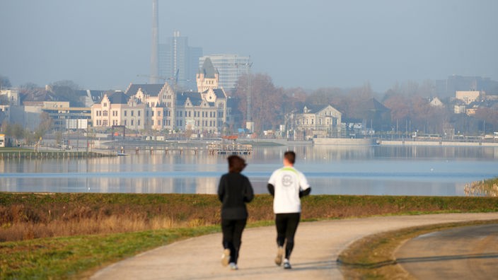 Zwei Jogger laufen am Donnerstag (17.11.2011) im Morgenlicht über die Uferpromenade des Phoenixsees in Dortmund. 