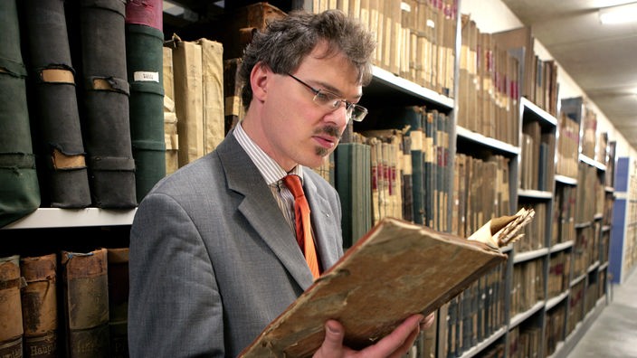 Ulrich Soénius mit einer Akte in der Hand, dahinter Regale voller Bücher