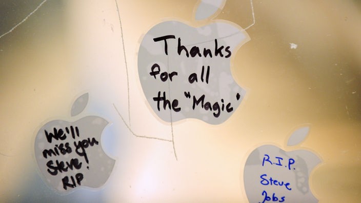 An der Scheibe eines Apple-Sores kleben Apple-Logos mit Widmungen der Fans für Steve Jobs