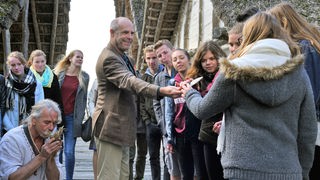 Herbert Zittlau (Peter Kremer, M. mit Komparsen), Leiter des Pfahlbaumuseums, zeigt Schülern historische Werkzeuge.
