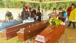 Drei Särge auf einem Friedhof in der brasilianischen Amazonas-Metropole Manaus. Angehörige mit Mund- und Nasenschutzmaske verabschieden sich.