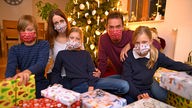 Eine Familie sitzt mit Mund-Nasen-Schutz vor dem geschmückten Weihnachtsbaum 