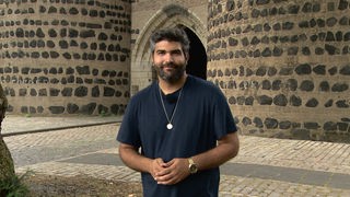 Hamzi steht vor einer alten Steinmauer